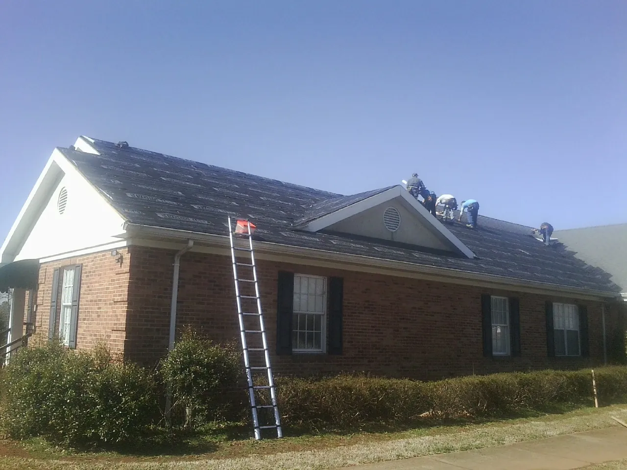 Crew tearing shingles off a brick ranch roof with a ladder set — Emergency Roof Repair work by our crew in Rapelje