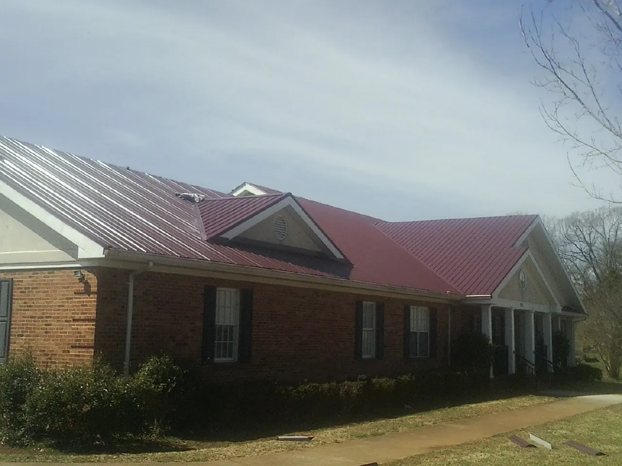 Red metal roof with gabled entries on a long brick building, from a Hail Damage Roof Repair job in Rapelje