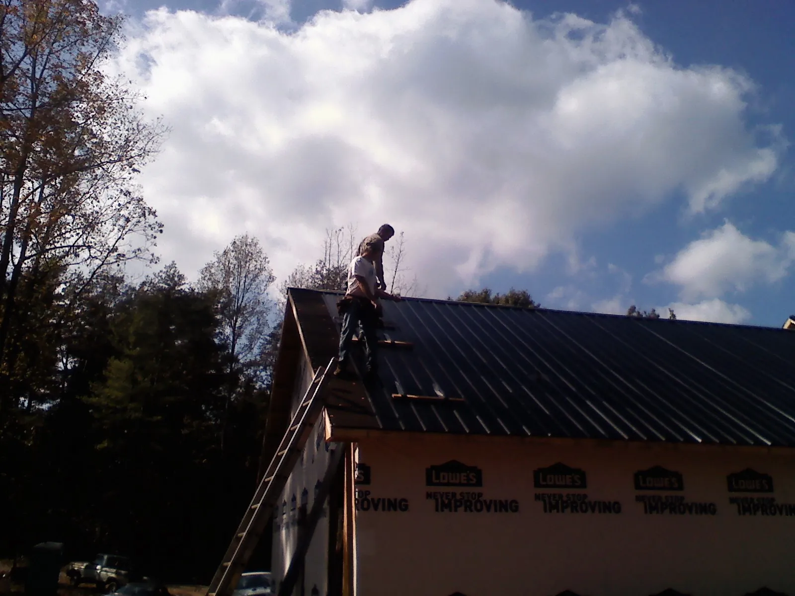 Roofer fastening dark metal panels high against a cloudy sky, from a Roof Inspection job in Rapelje