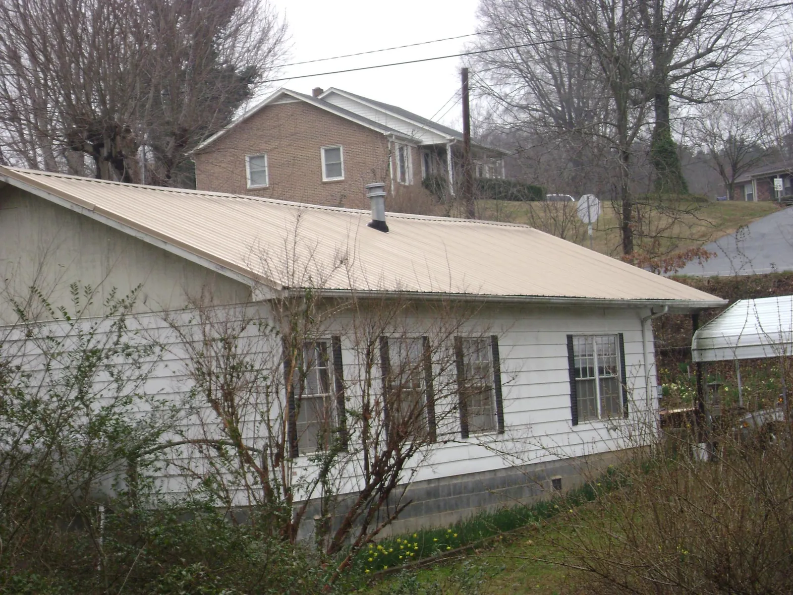 Tan metal roof on a white sided house set into a hillside — Commercial Roofing by Roofing Brothers in Rapelje